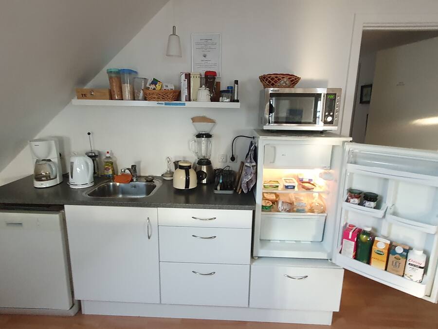 Cocina compacta equipada con microondas, cafetera y refrigerador lleno de bebidas.