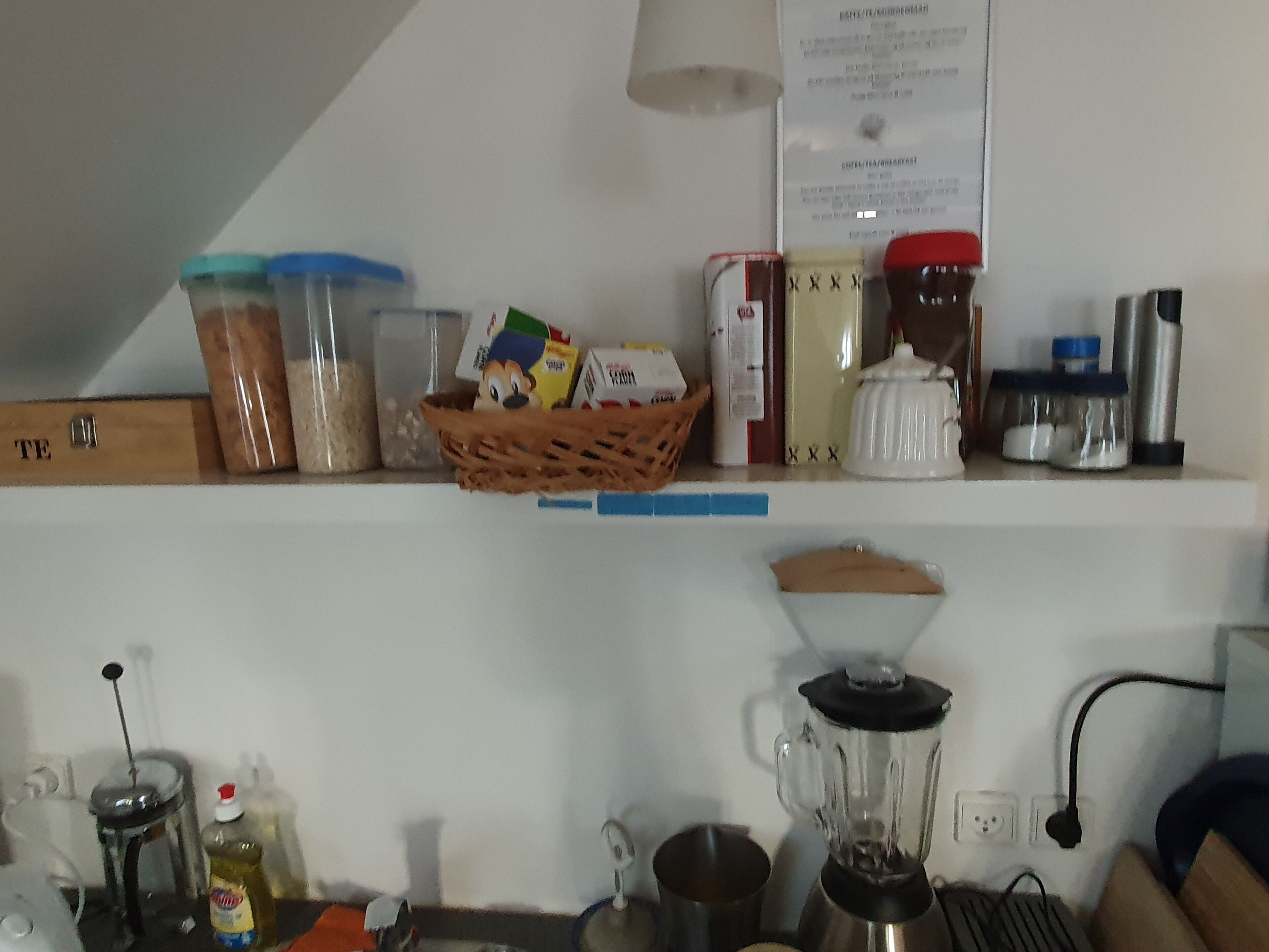 A kitchen counter with various kitchen items, including jars, a blender, and a basket with food items.
