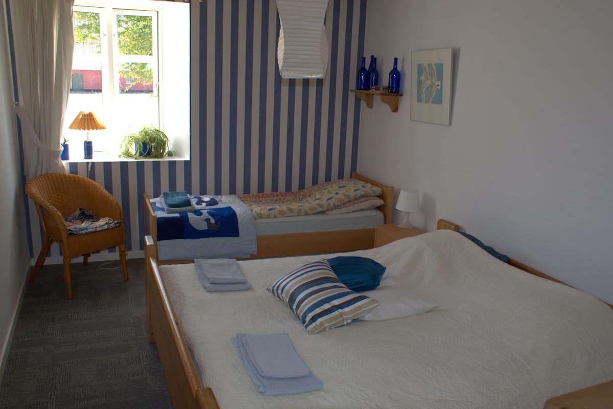 A bedroom with two single beds, a chair, a table with a lamp, and a window with curtains.