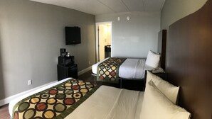 Una habitación de hotel con dos camas, cafetera, televisión y puerta que da a un baño.