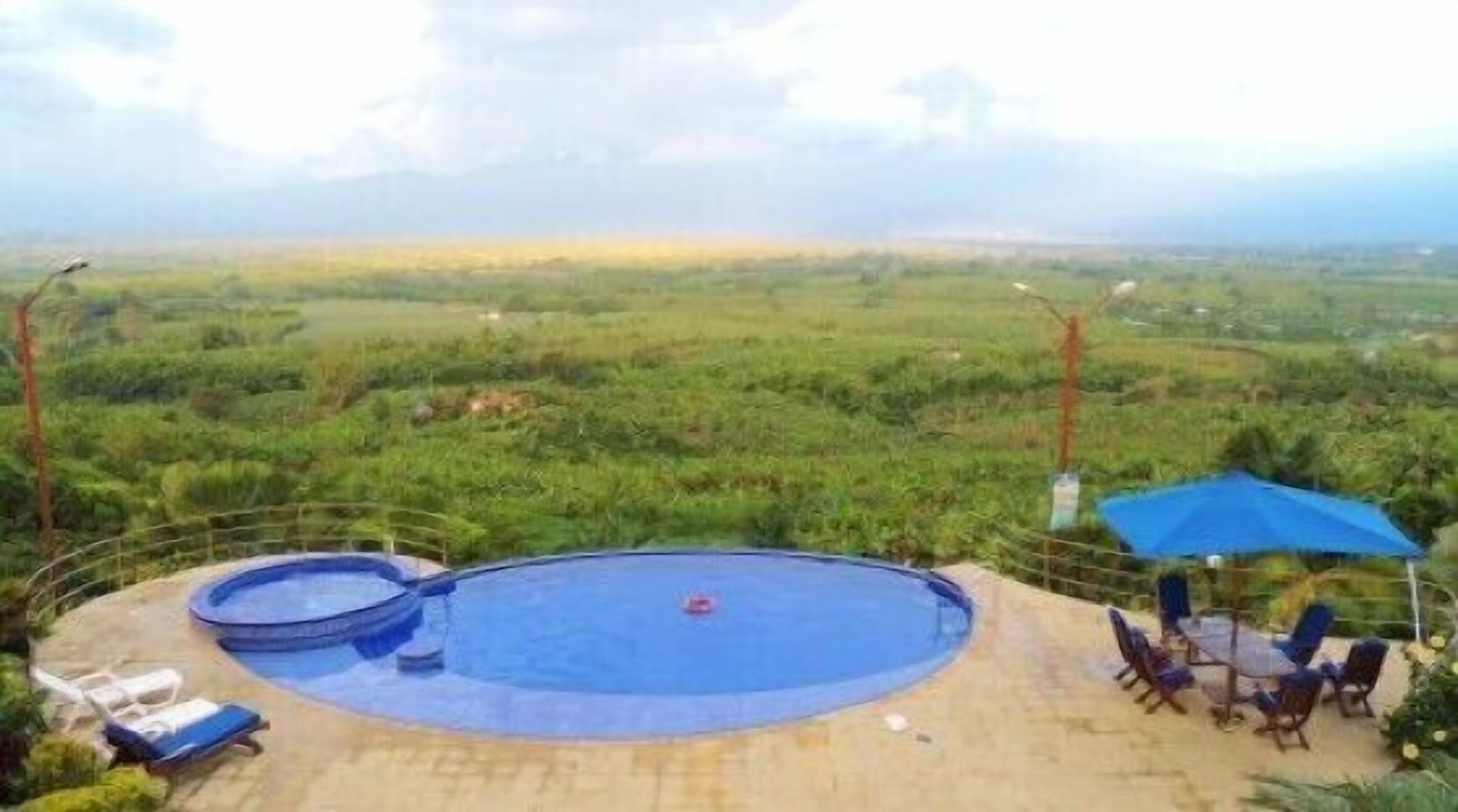 A pool with lounge chairs and an umbrella, surrounded by a view of a green landscape.