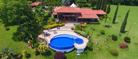Une grande maison avec une piscine, entourée de jardins bien entretenus et de grands arbres.