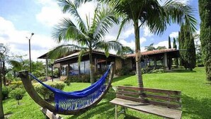 A hammock, a wooden bench, and a house with a thatched roof in a grassy area with palm trees. - Finca Hotel La Tata Premium (Montenegro)