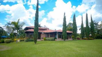 A building with a red-tiled roof, surrounded by a well-maintained lawn and tall trees.