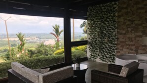 A room with wicker furniture, a view of greenery and mountains, and a stone wall with a plant grid. - Finca Hotel La Tata Premium (Montenegro)