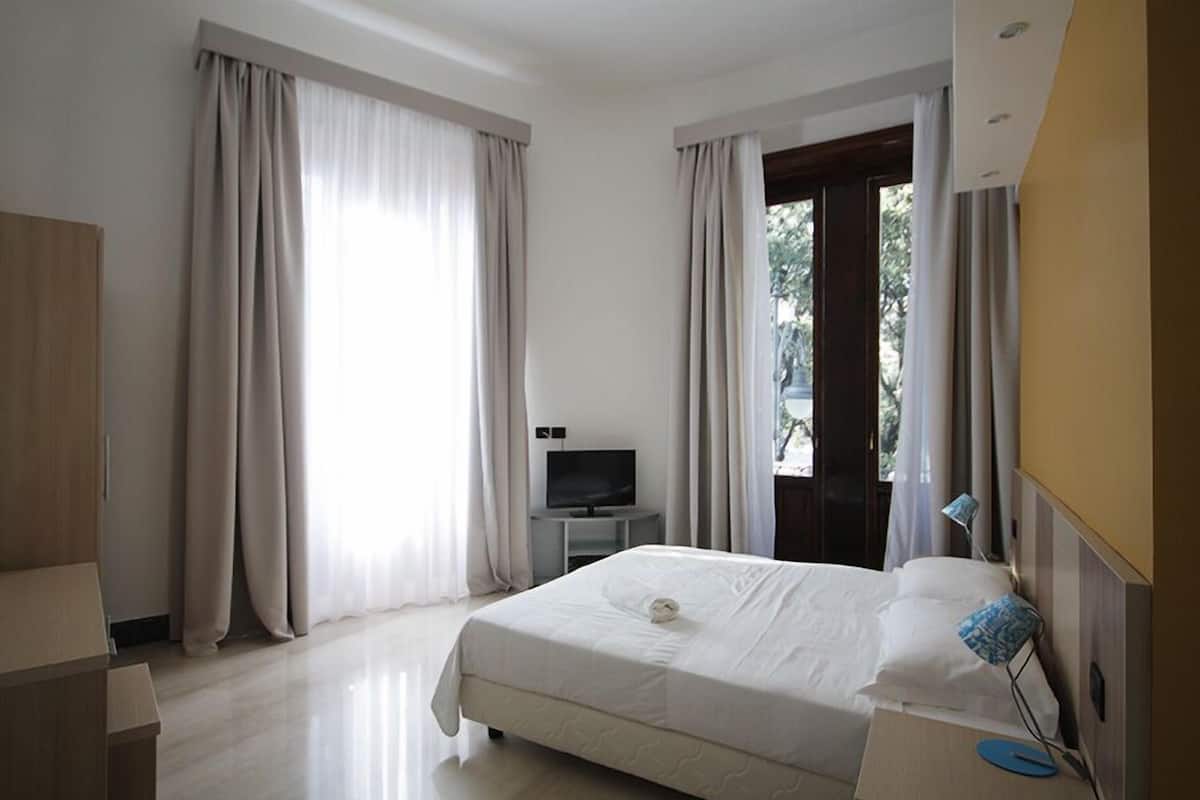 A hotel room with a bed, a TV, a desk, and curtains.