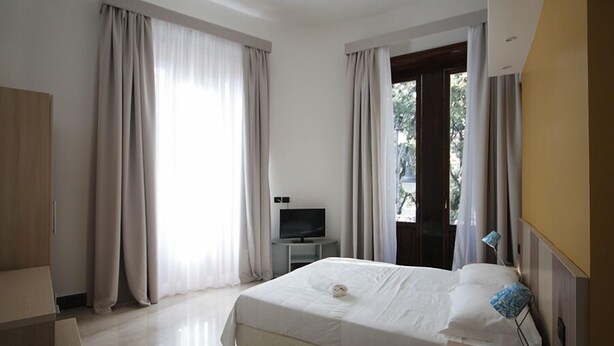 A hotel room with a bed, a TV, a desk, and curtains.