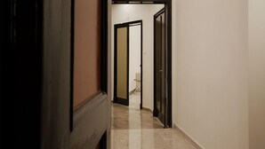 A hallway with a door leading to a room. The hallway has a tiled floor and plain walls.
