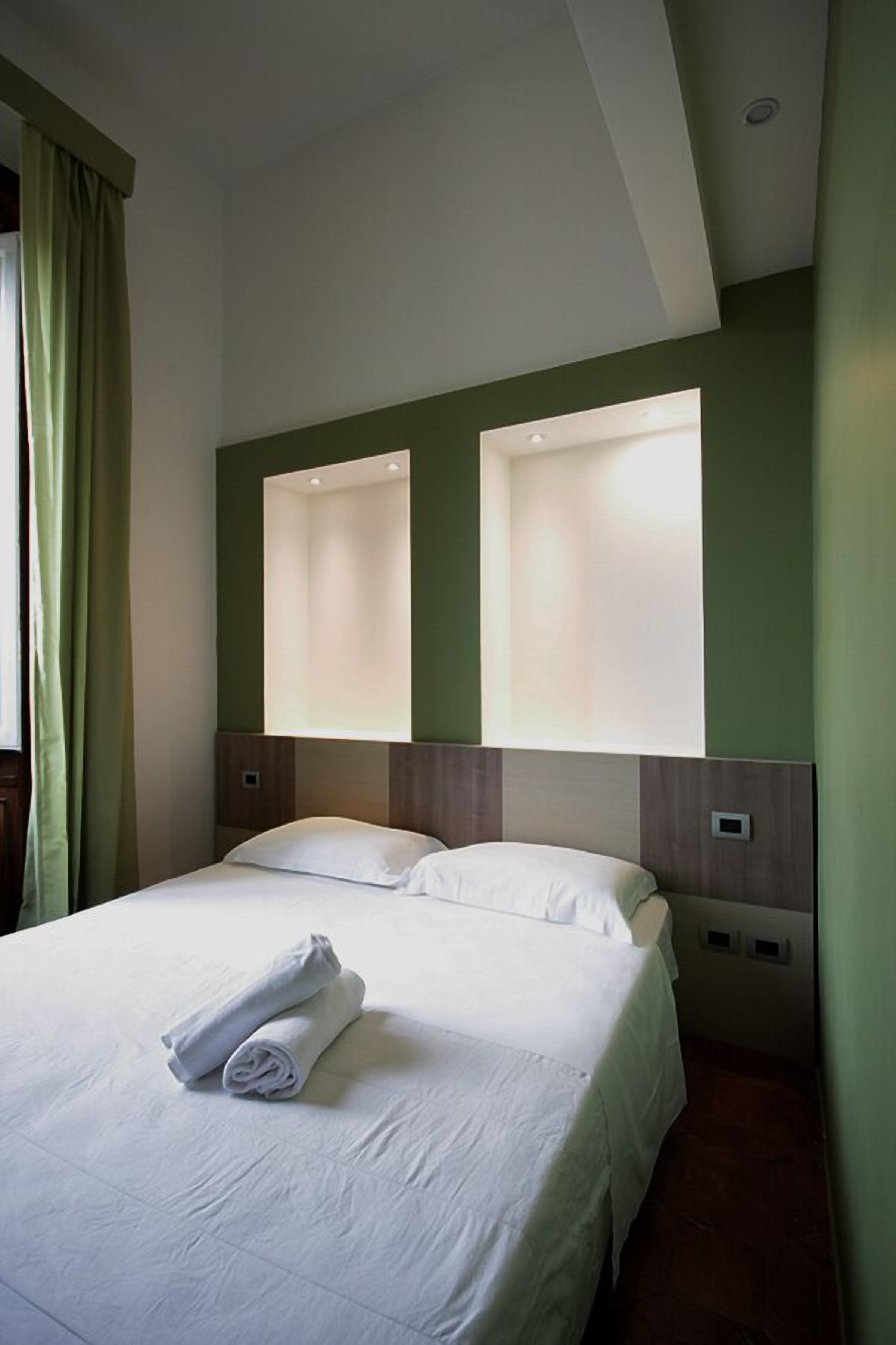 A hotel room with a neatly made bed, two bedside tables, and a large window with curtains.