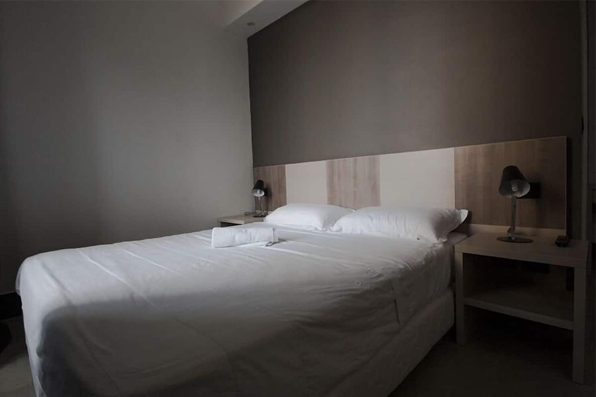 A modern hotel room with a large bed, two bedside tables with lamps, and a neutral color scheme.