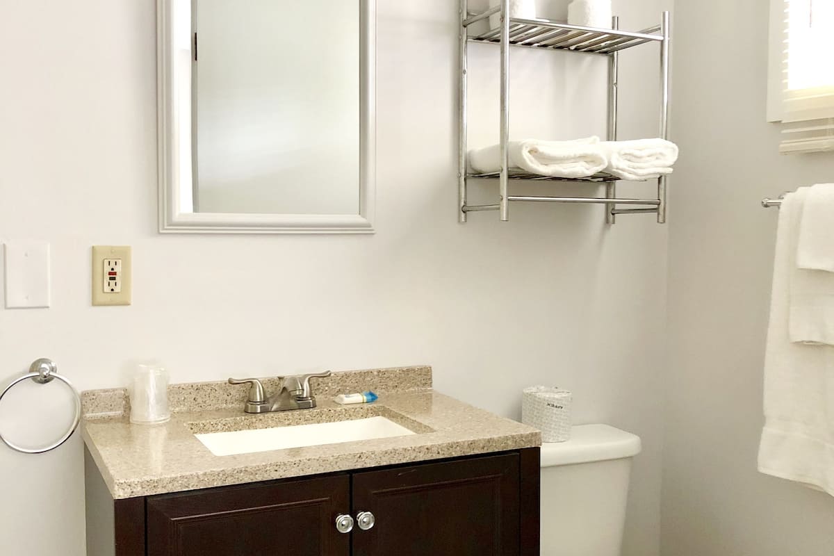 A bathroom with a white sink, dark wooden vanity, a mirror, a toilet, and a towel rack.
