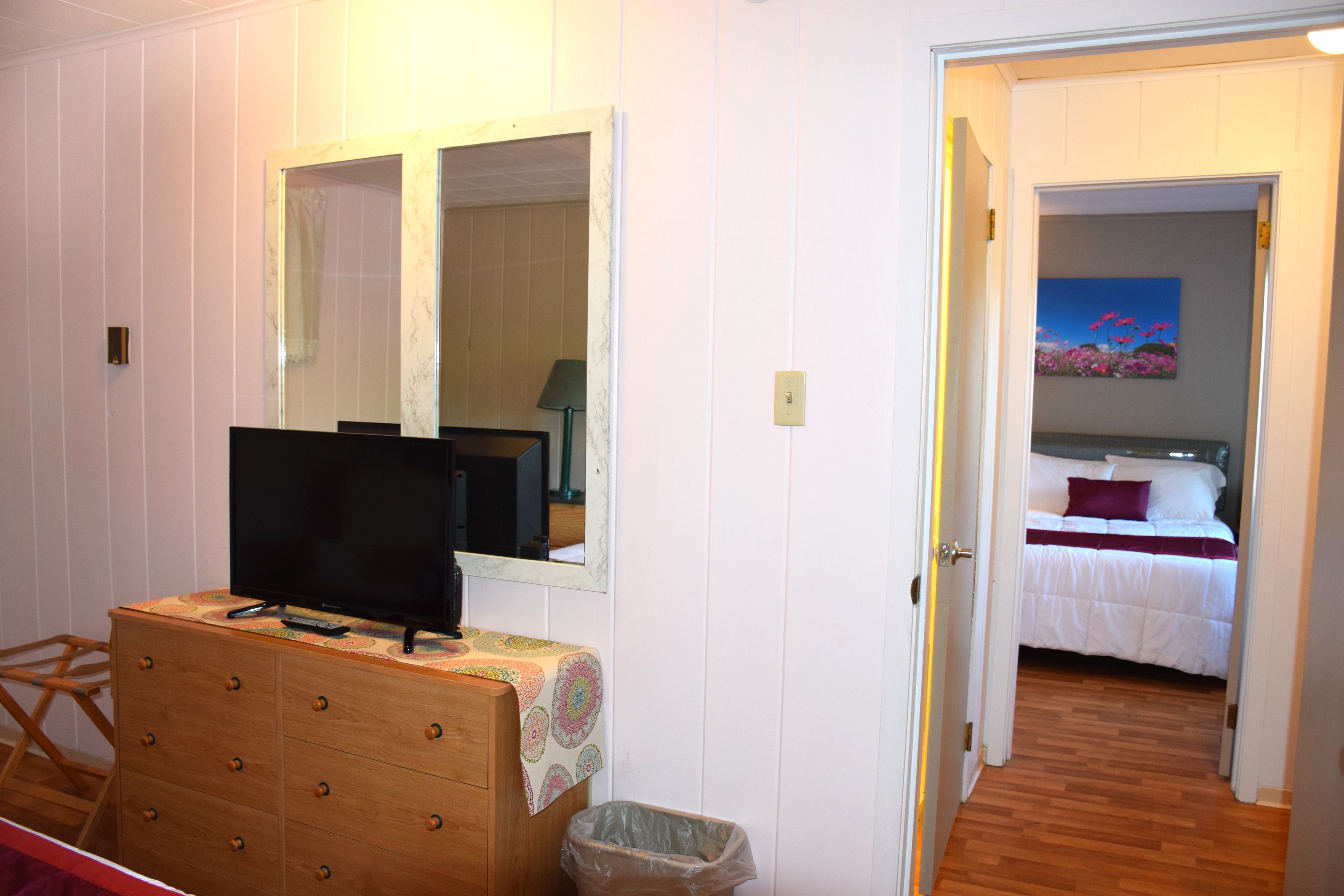 A bedroom with a wooden dresser, a television, a mirror, and a painting on the wall.