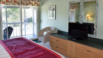 A bedroom with a bed, a dresser, a television, a chair, and a window with a view of greenery.
