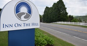 Cartell de 'Inn On The Hill' amb un logotip, un camí i vegetació al fons.