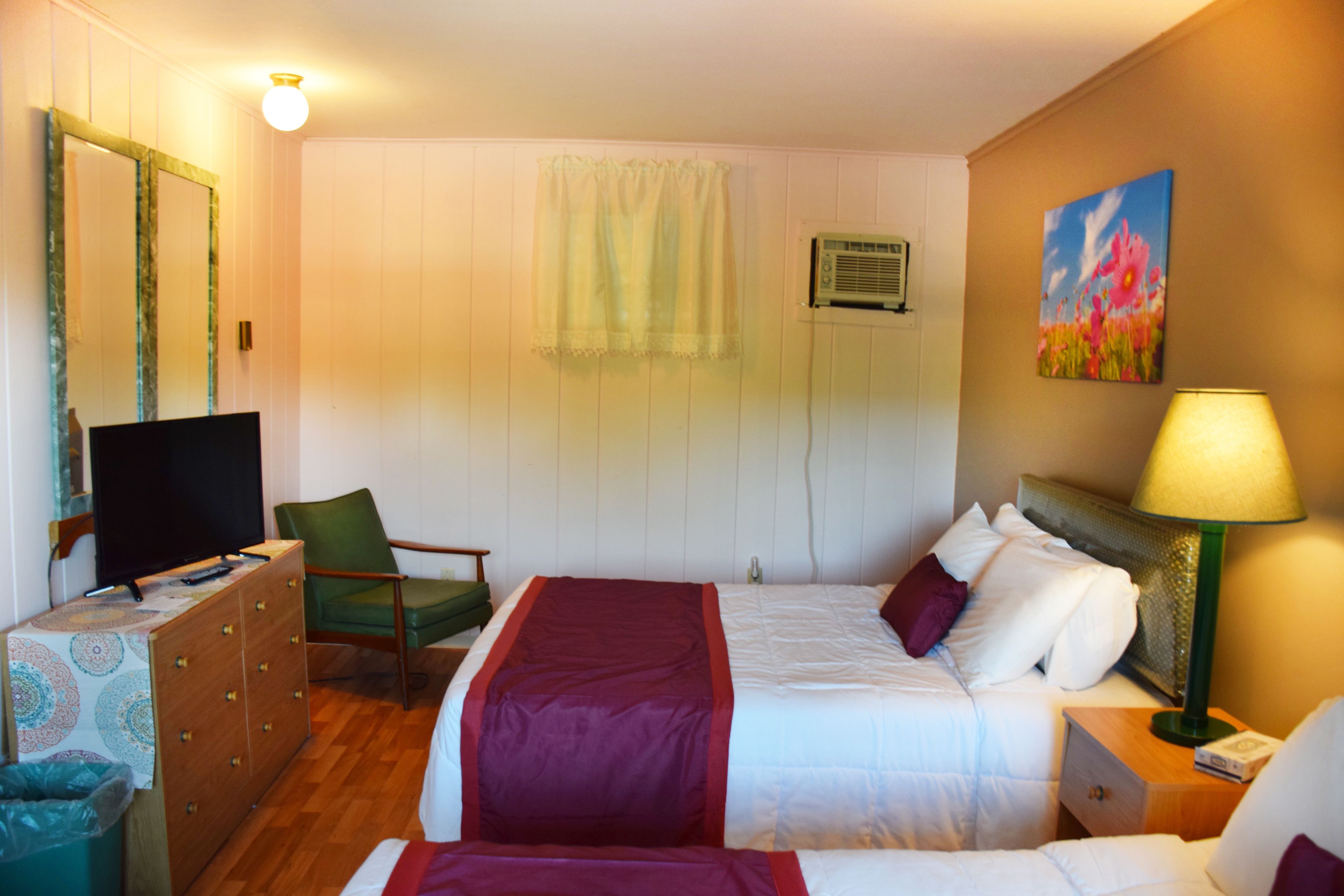 A hotel room with a bed, a dresser, a television, a chair, a lamp, and a painting on the wall.