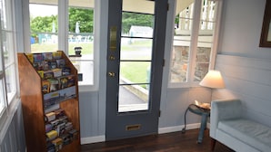 A wooden bookcase filled with books, a blue door with a window, a lamp, and a light blue armchair. - Inn on the Hill (Lake George)