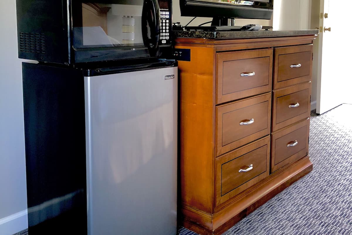 A compact kitchenette with a refrigerator, microwave, and a television on a wooden cabinet.