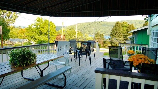 A covered outdoor seating area with wooden benches and chairs, overlooking a residential neighborhood and a lake. - Inn on the Hill (Lake George)