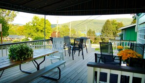 A covered outdoor seating area with wooden benches and chairs, overlooking a residential neighborhood and a lake. - Inn on the Hill (Lake George)