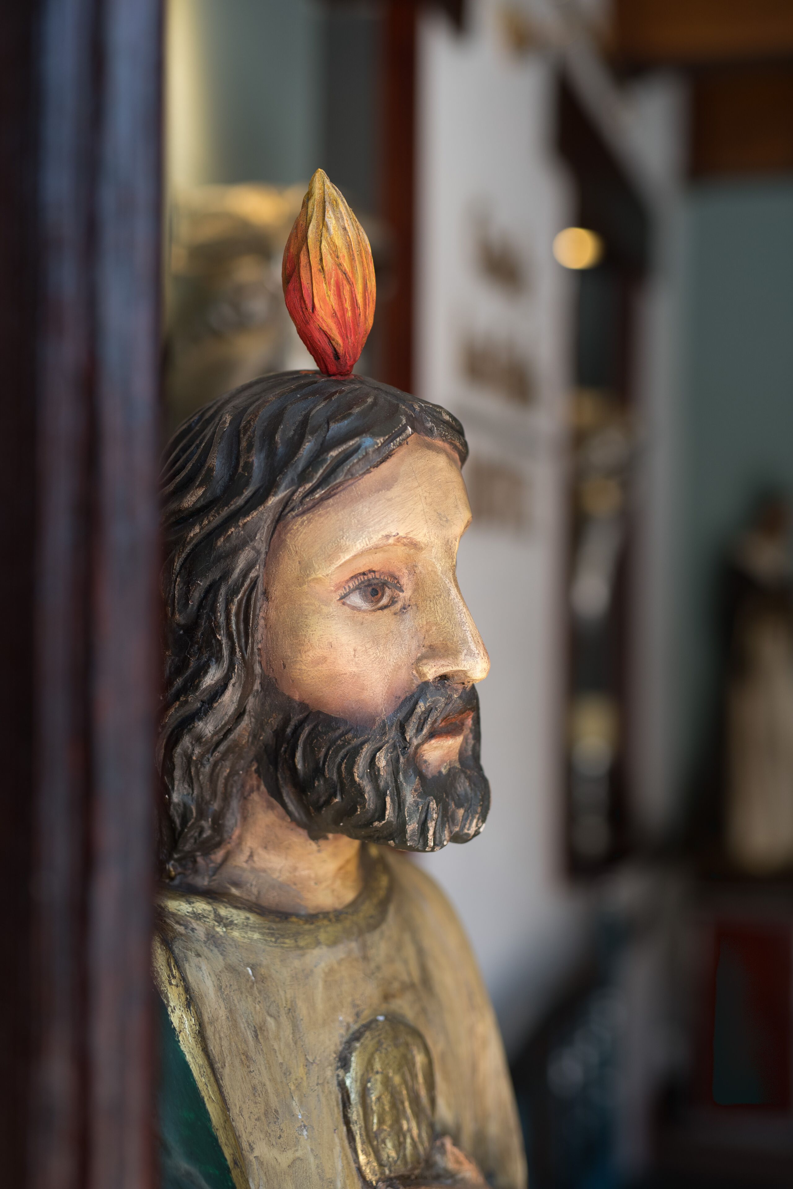 Une statue en bois surmontée d’une flamme, placée sur un fond flou.