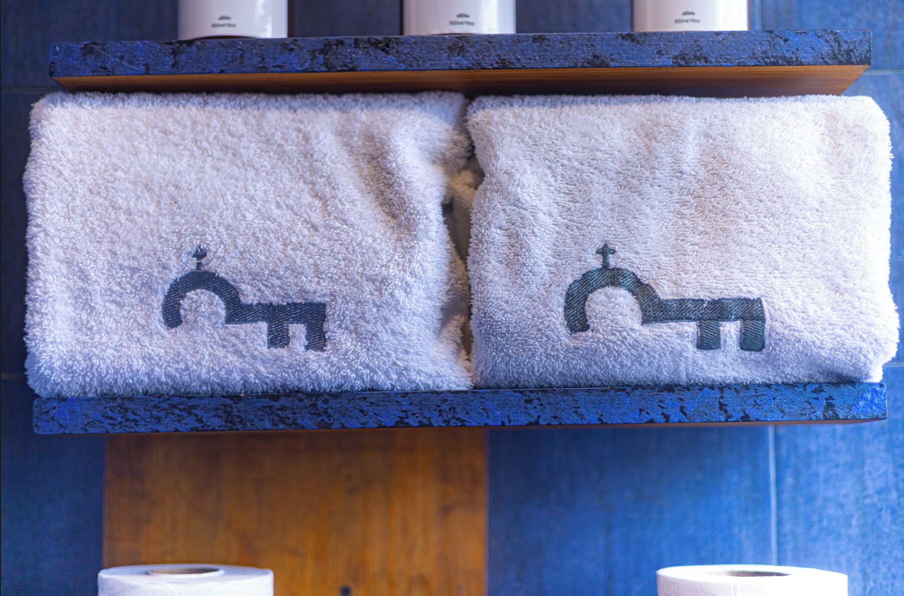 Two towels with a faucet and horse icon on a wooden shelf.