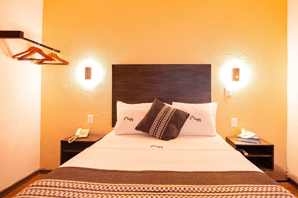 A hotel room with a bed, two bedside tables, a telephone, a tissue box, and a hanging coat rack.
