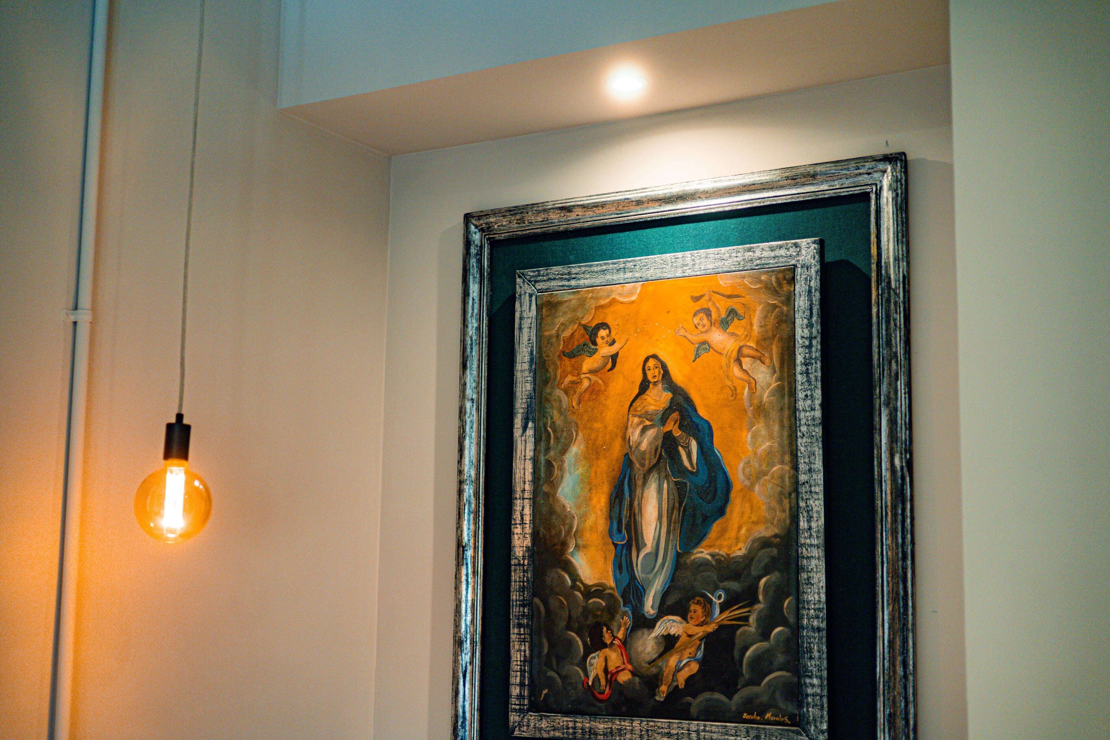 A framed artwork with a religious figure, a light bulb, and a wall.