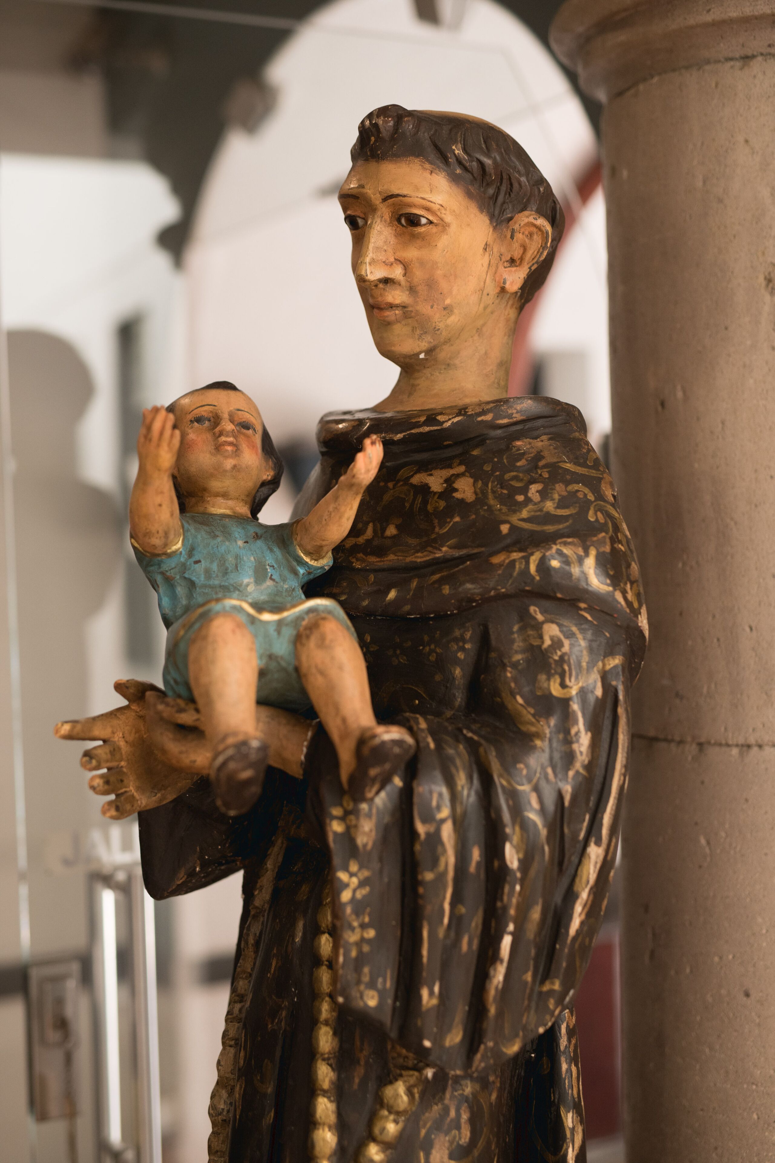 Estátua de uma figura segurando uma criança, diante de uma coluna.
