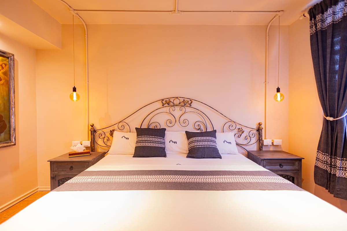 A neatly made bed with a metal headboard, two bedside tables with lamps, and a painting on the wall.