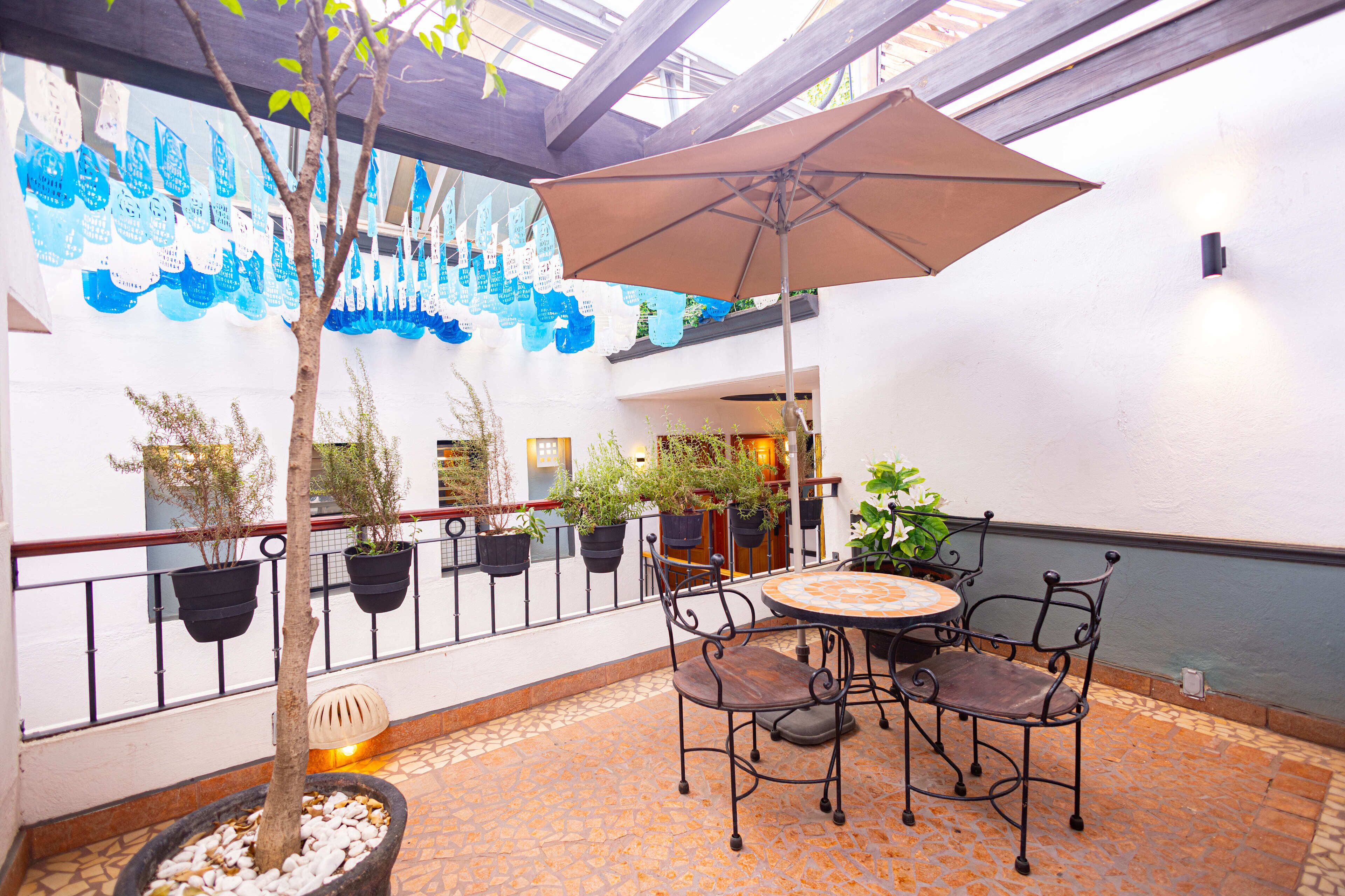 An outdoor patio area with a round table and chairs, surrounded by potted plants and a decorative wall mural.