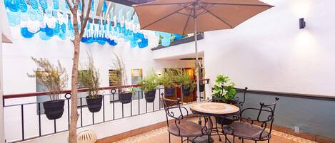 An outdoor patio area with a round table and chairs, surrounded by potted plants and a decorative wall mural.