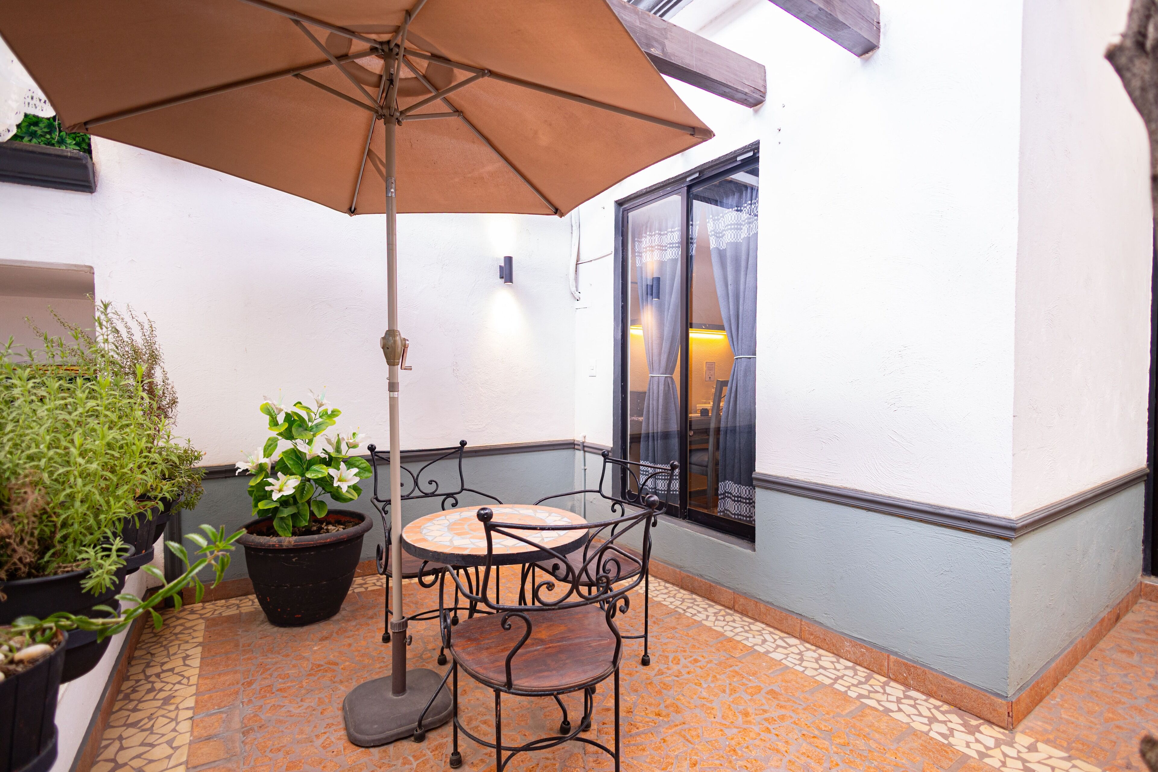 A patio with a table and chair, a potted plant, and an umbrella.