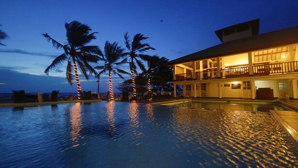 A swimming pool with palm trees and a building with a balcony.