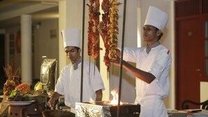 Chefs preparing food in a kitchen with a large grill and various cooking utensils.