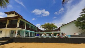 A hotel with a pool area, lounge chairs, and a sandy beach.