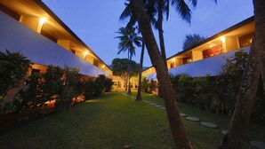 A hotel courtyard at dusk with a well-maintained lawn, palm trees, and a stone pathway leading to the building.