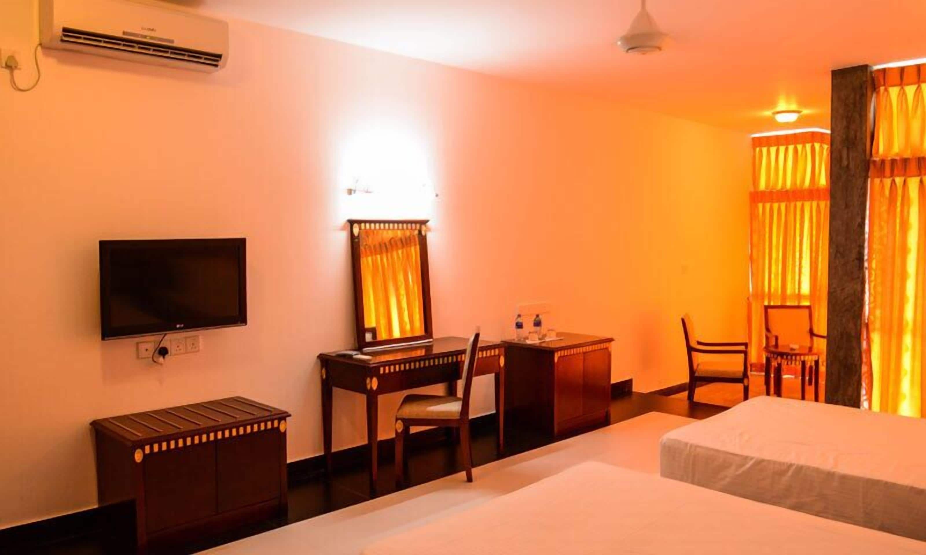 A hotel room with a bed, a desk with a chair, a television, and an air conditioning unit.