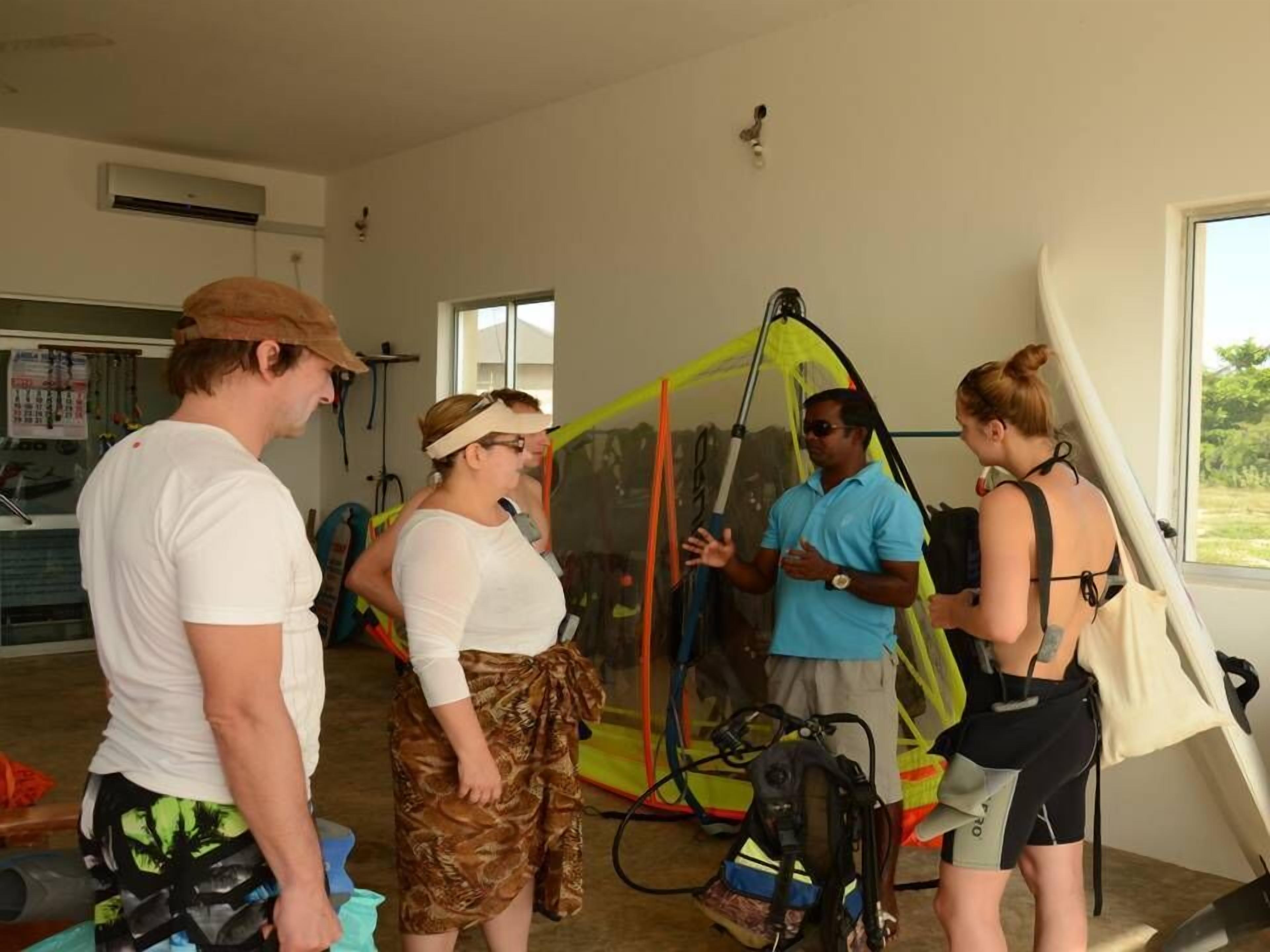 A group of people in a room with a large window, a ceiling fan, and a visible air conditioning unit.