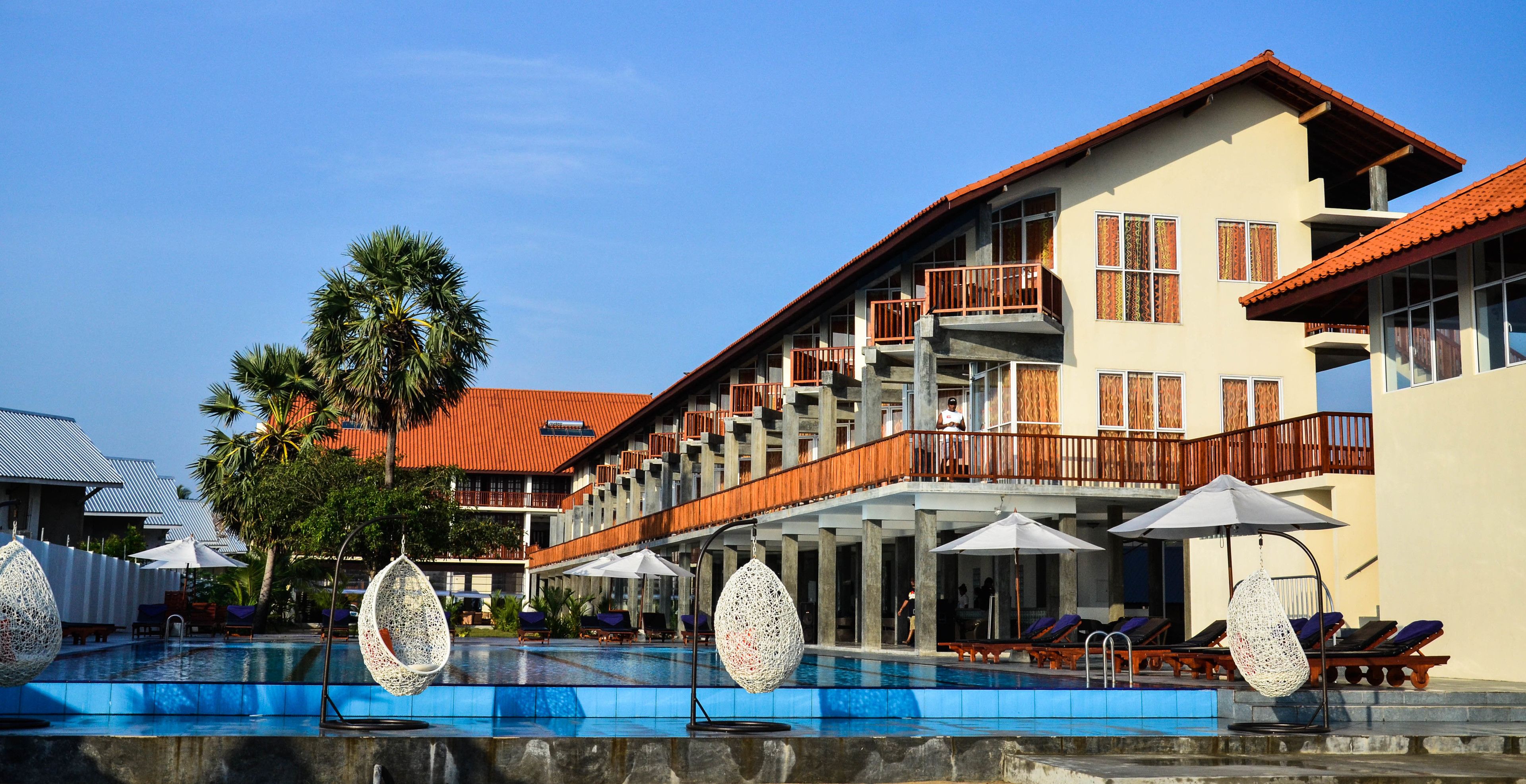 A hotel with a swimming pool, outdoor seating, and a multi-story building with balconies.