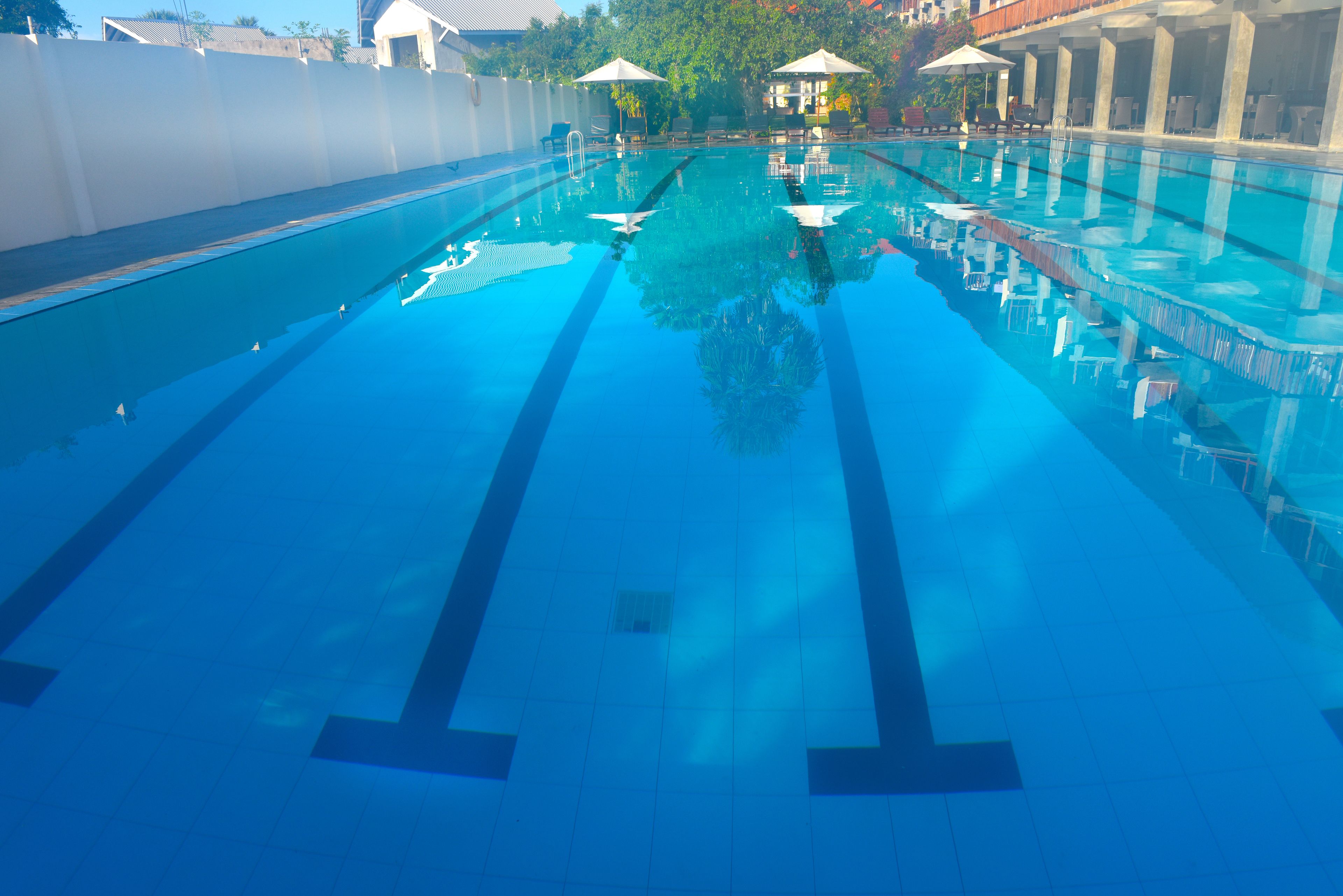 A clear swimming pool with lane dividers, lounge chairs, and umbrellas.