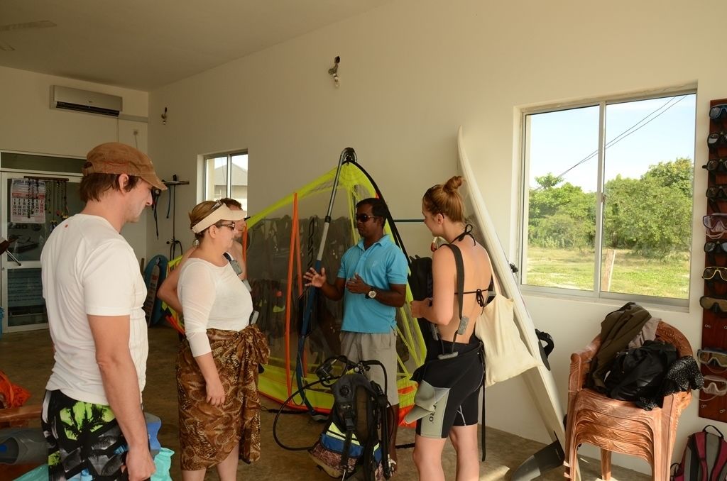 A group of people in a room with a large window, a chair, and a surfboard.