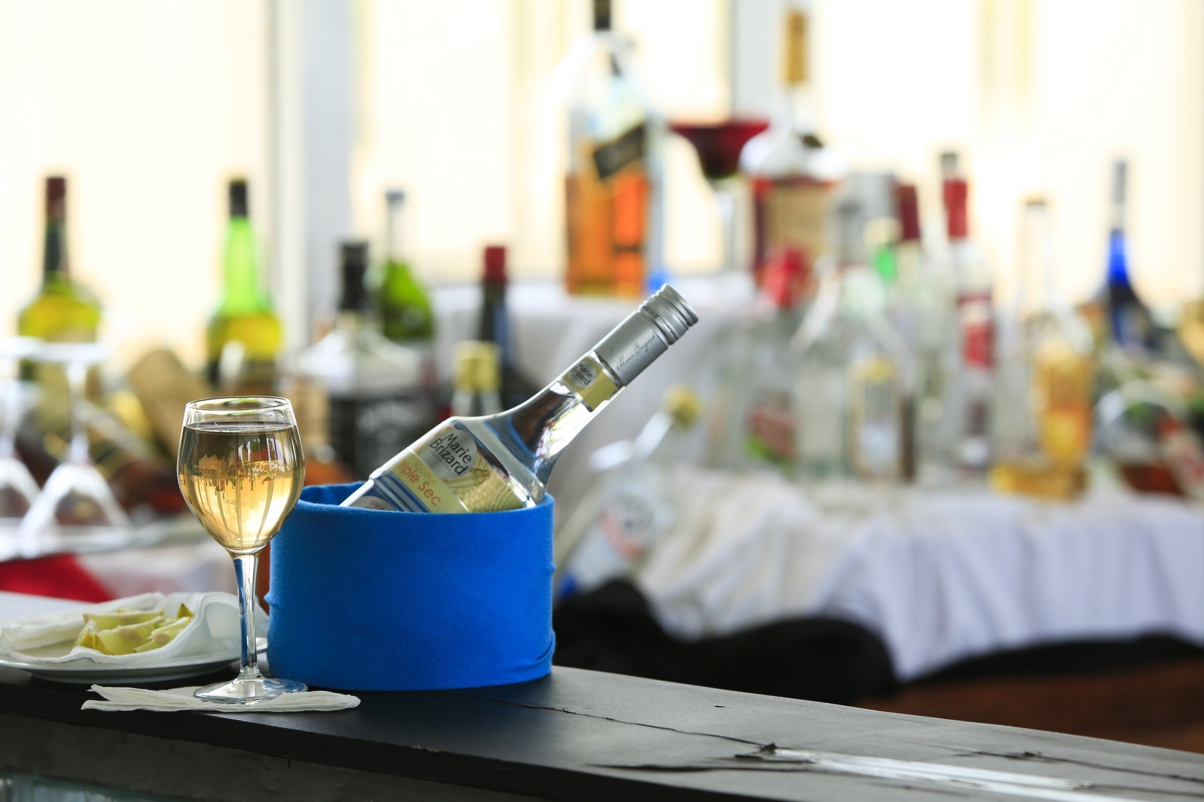Un bar con una copa de vino blanco y una botella en un soporte azul.