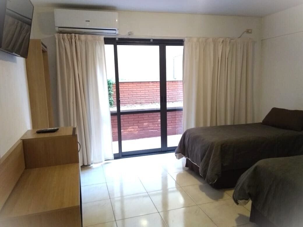 A hotel room with a bed, a desk, and a sliding glass door leading to an outdoor area.