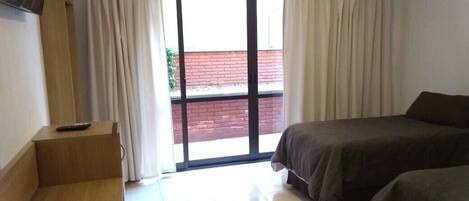 A hotel room with a bed, a desk, and a sliding glass door leading to an outdoor area.