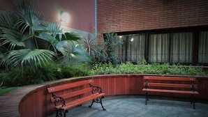 Un patio con dos bancos de madera, un muro de ladrillo y una ventana con cortinas.