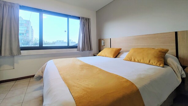 Habitación de hotel con una cama grande, dos almohadas, una ventana con cortinas y vistas a edificios.