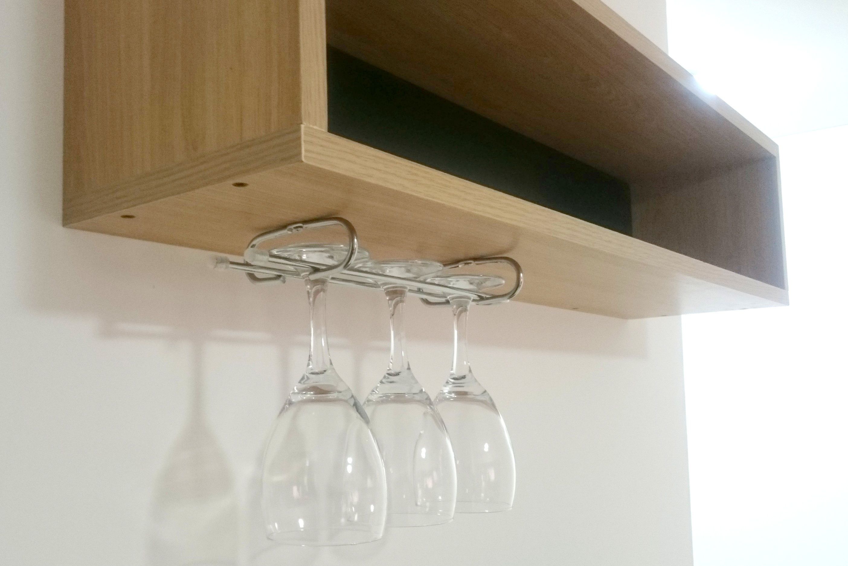A wooden shelf with three wine glasses hanging from a metal hook.