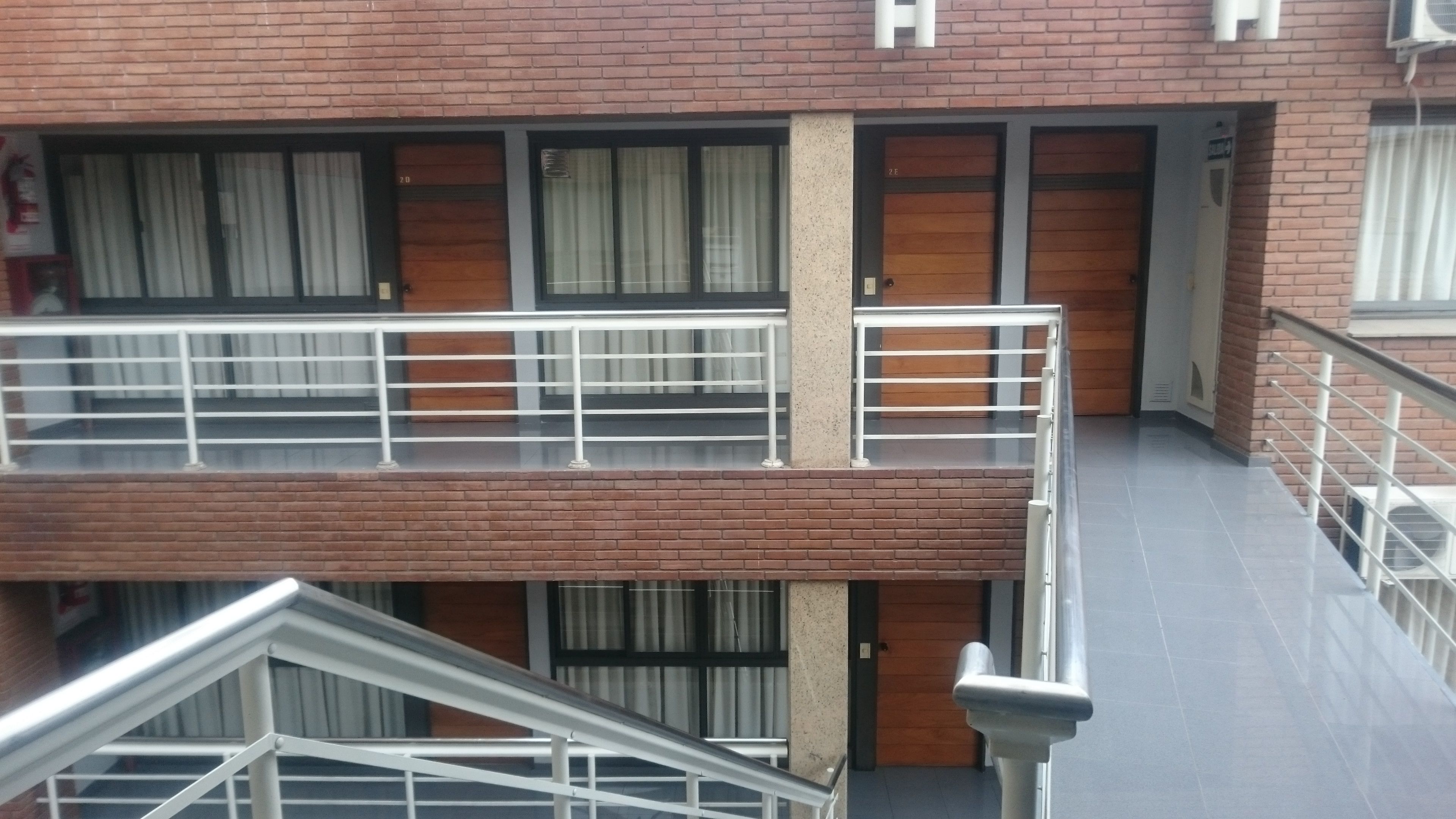 A multi-story building with a brick facade, balconies with metal railings, and large windows with curtains.