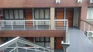 A multi-story building with a brick facade, balconies with metal railings, and large windows with curtains.