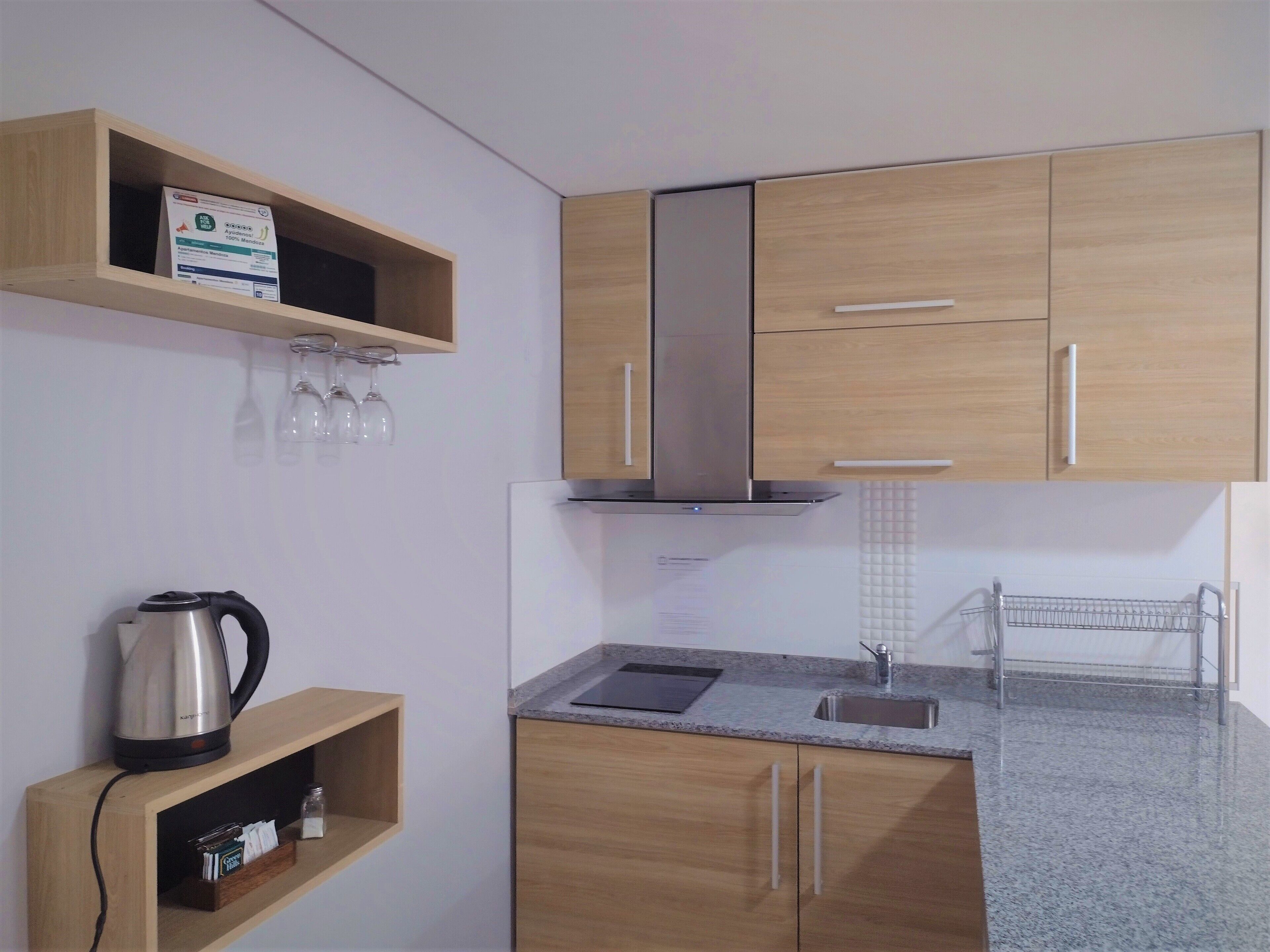 A modern kitchen with wooden cabinets, a stainless steel range hood, a built-in sink, and a kettle on a shelf.